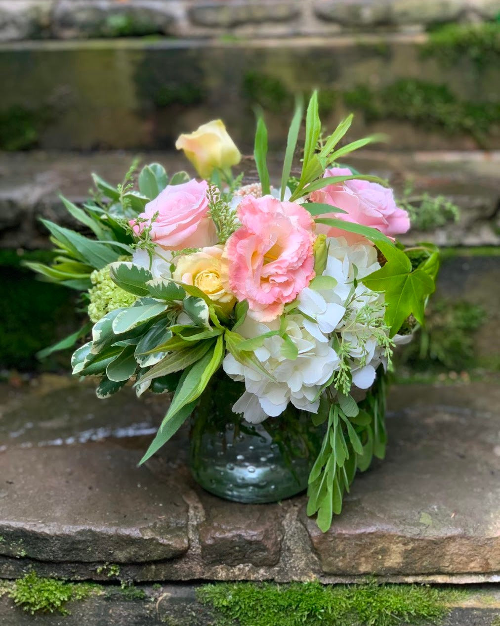 Bouquet of flowers in a green vase on stone steps with a natural background