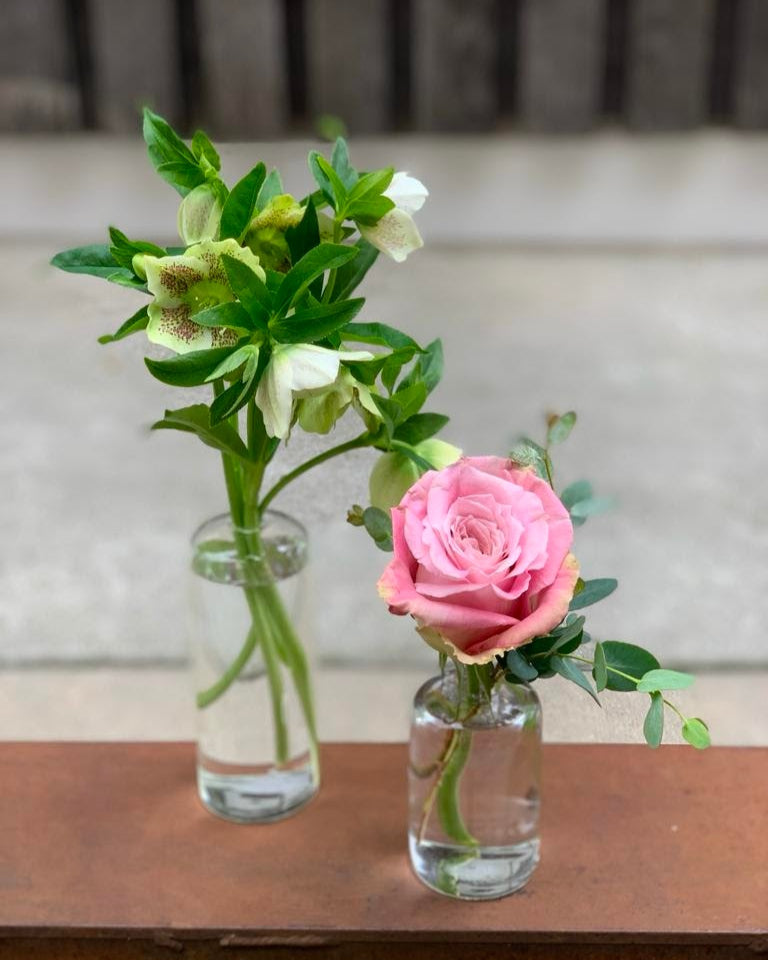 Two small glass vases with flowers on a wooden surface.