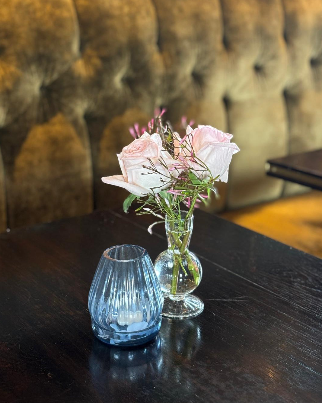 Floral arrangement in a glass vase on a wooden table with a brown upholstered booth in the background.