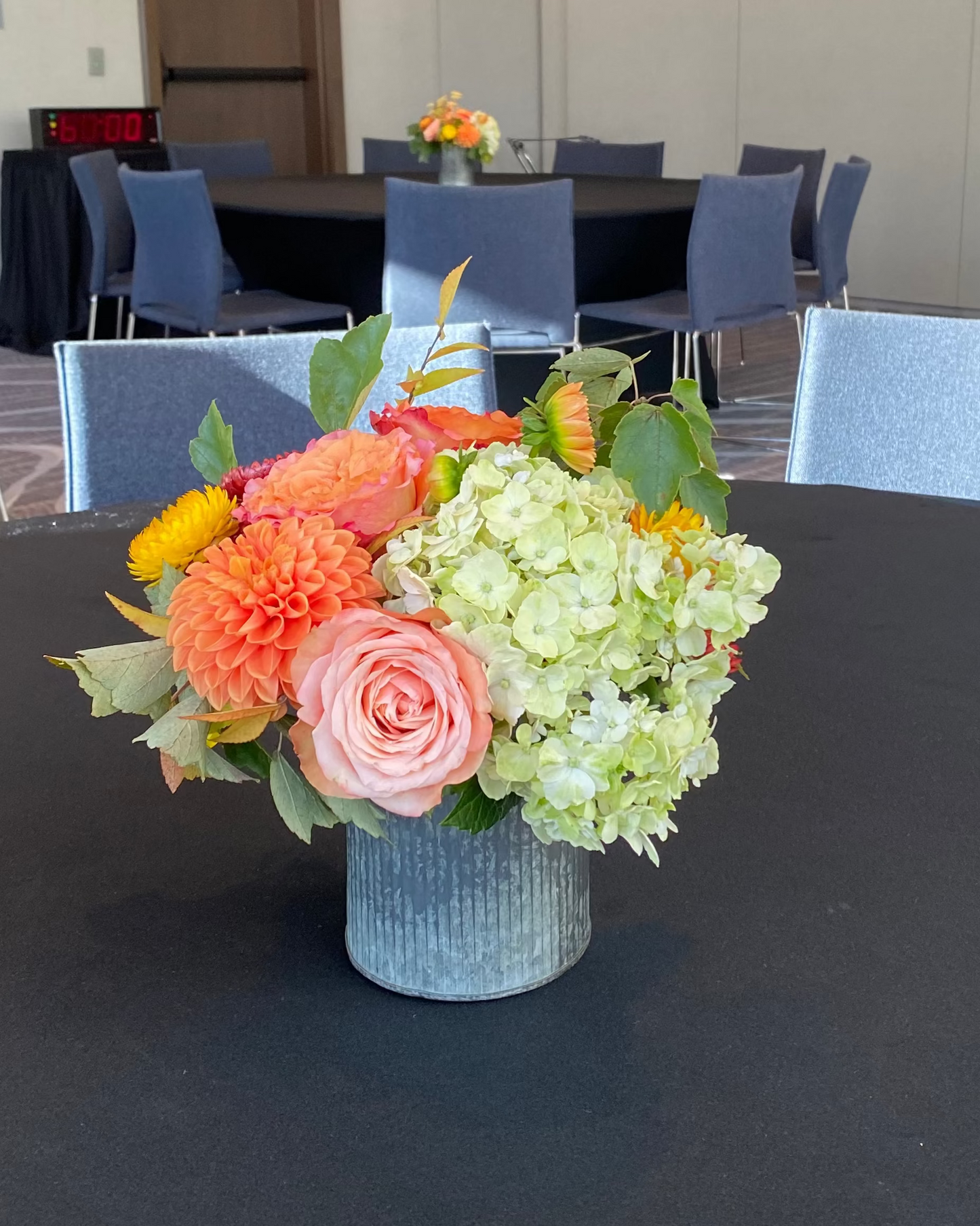 Floral arrangement on a table in a conference room with chairs and tables in the background.