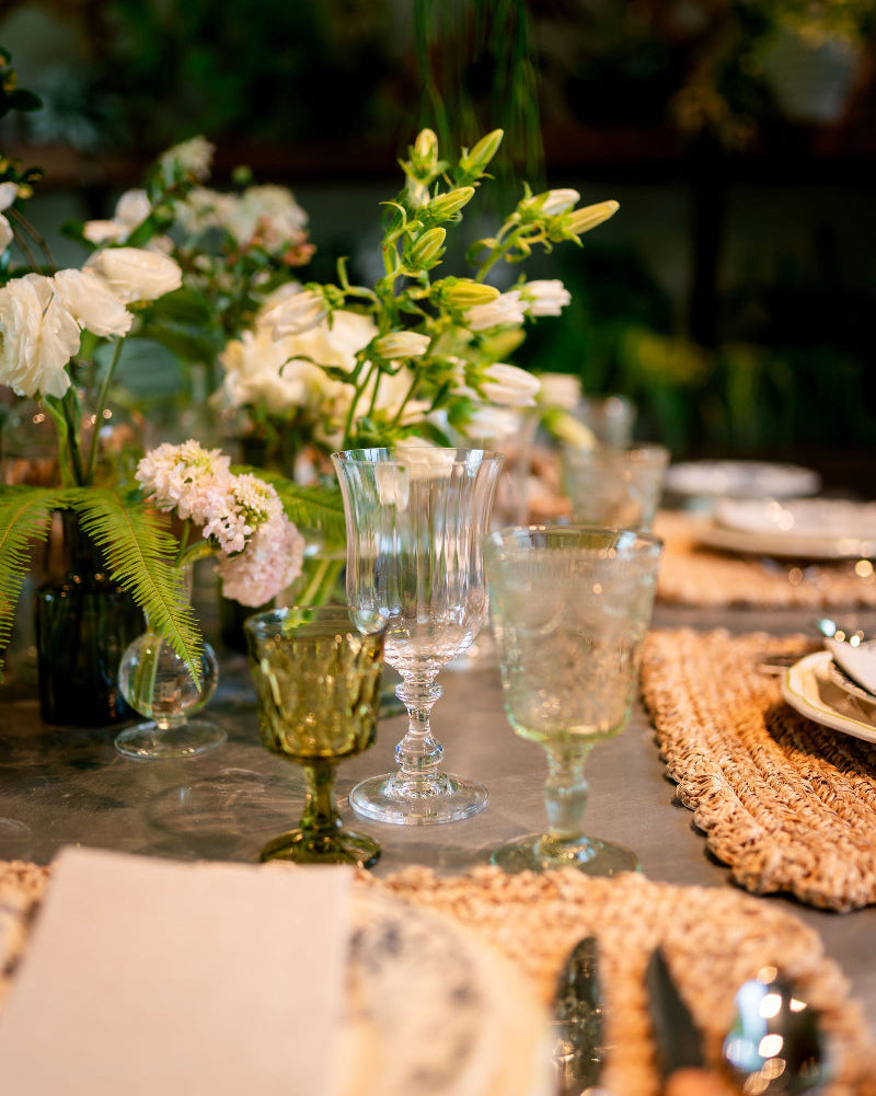 Elegant table setting with floral arrangements, glasses, and plates on a reflective surface.